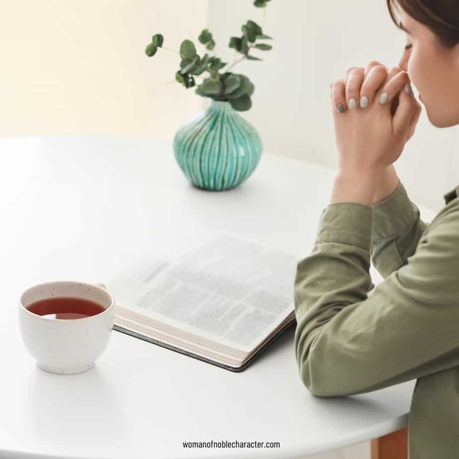 image of a woman praying with an open bible on the table for the post She Opens Her Mouth With Wisdom Proverbs 31:26 Today