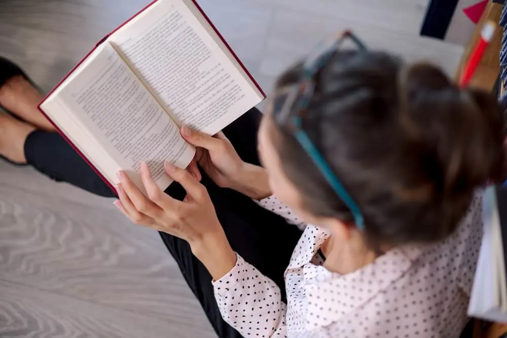 Top view of beautiful woman wearing and pink pale shirt, holding a book touching the pages with fingers, sitting on the floor and reading a book in the book shop.; Bible character study worksheet