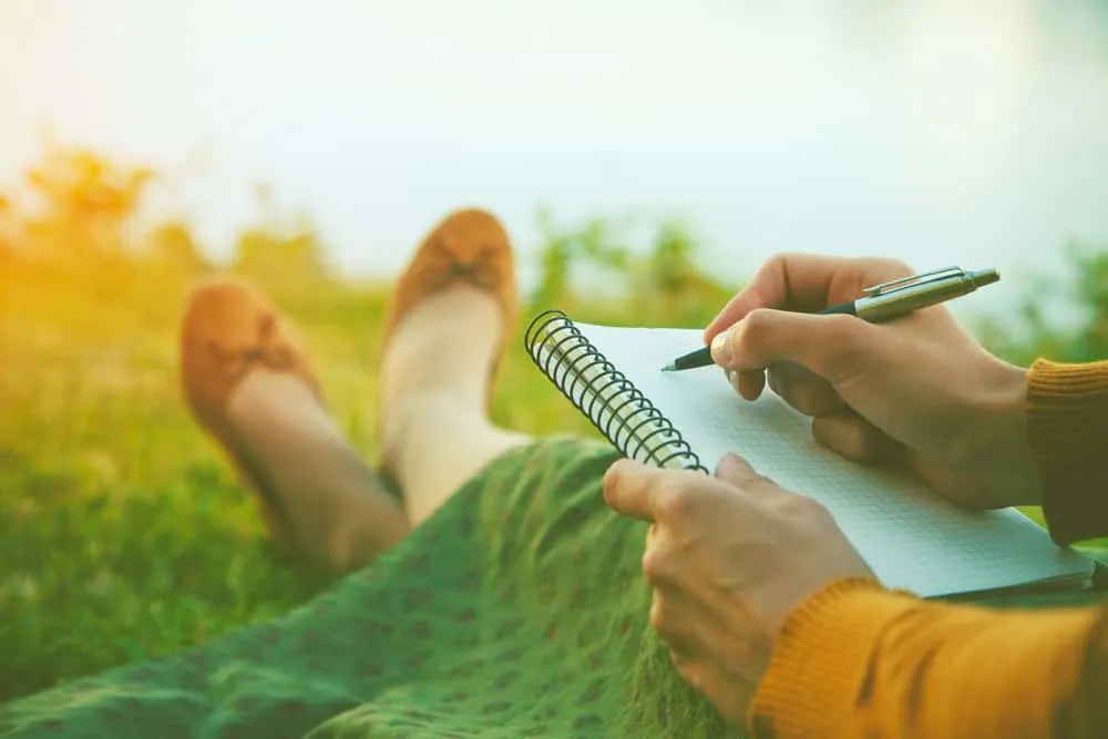 female hands with pen writing on notebook on grass outside; getting closer to God