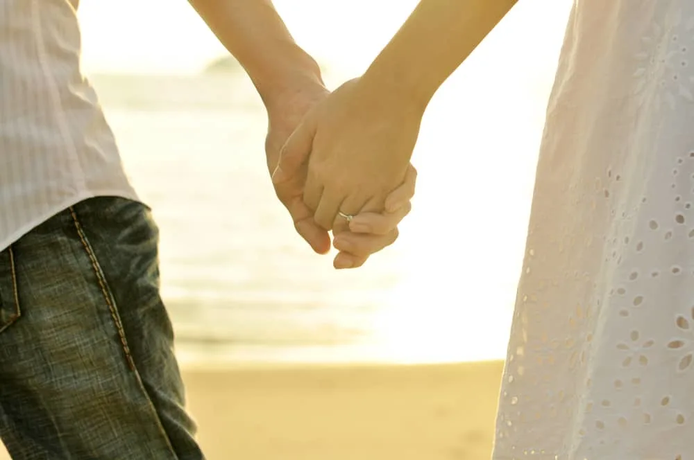 Young adult male and female holding hands on beach at sunset.; how i led my husband bck to God