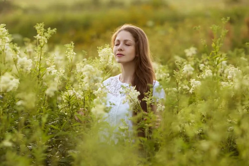 Happy young woman with eyes closed among the wildflowers; meek and gentle spirit