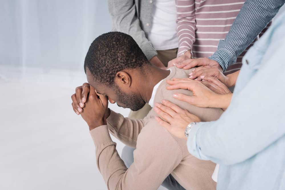 image of man with people laying hands on him and praying for the post on prayer for addiction