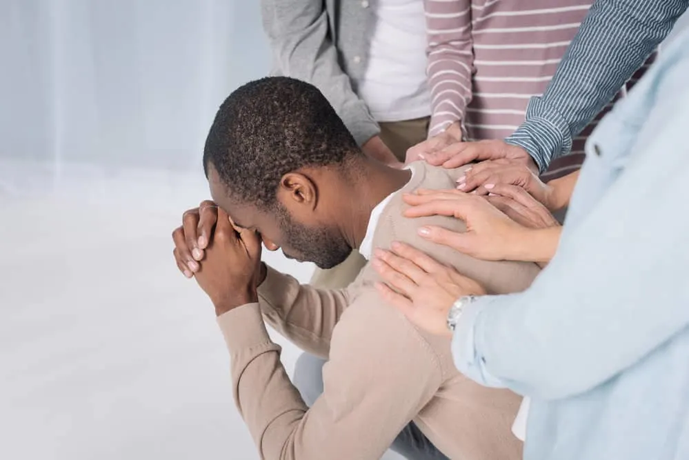 image of man with people laying hands on him and praying for the post on prayer for addiction