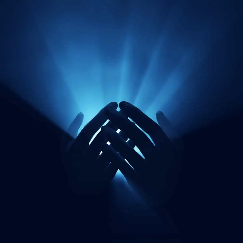 image of praying hands in the dark for the post How to Pray in the Midst of Spiritual Warfare