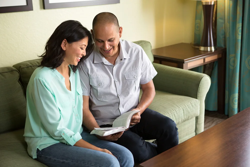 Happy couple sitting on the sofa reading the Bible. for the post how to be a godly wife