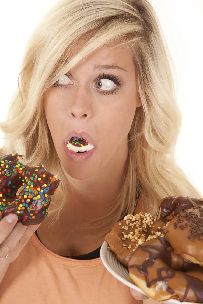 a woman with a plate full of doughnuts and also a mouth full of a doughnut. for the post on the 7 deadly sins