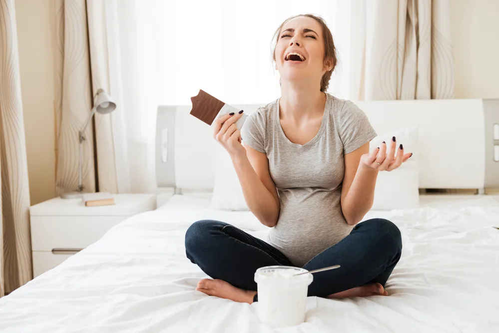 image of pregnant mother on bed eating chocolate for the post on prayer for pregnant mothers